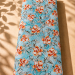 Charming rose print featuring warm orange and ivory blooms with soft grey foliage on a refreshing aqua-blue background.