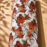 Watercolor-inspired floral print featuring bold burnt-orange blossoms with artistic green and charcoal accents on a soft ivory background.