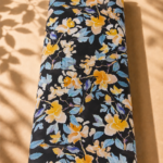 Elegant floral print featuring golden-yellow blossoms and soft blue leaves on a deep black background.