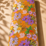 Tropical-inspired floral design featuring purple, white, and soft pink blossoms with lush green foliage on a vibrant orange background - SWISS COTTON (PC01)