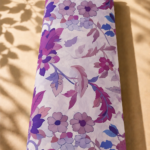 Stylized botanical print featuring layered blossoms and sweeping leafy branches in plum, violet, mauve, and blue tones on a soft ivory base - SWISS COTTON (PC01)