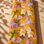 Vibrant orange cotton featuring tropical floral motifs in purple, soft pink, white, and yellow, accented with lush green leaves - Italian Cotton (PC02)