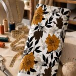 Elegant floral fabric featuring bold golden blooms with deep brown flowers and black leafy accents on a soft ivory background.