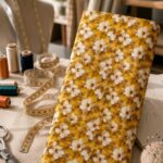 Charming floral fabric featuring delicate ivory blooms over a rich golden yellow background.