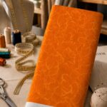 Tonal floral design featuring delicate oversized flower outlines in soft golden-orange over a vibrant orange background.