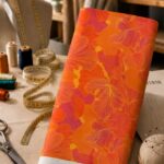 Bold oversized floral design in vivid coral, pink, and orange tones over a vibrant orange background, creating a striking tonal look.