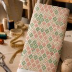 Delicate mini florals in dusty pink, soft green, and ivory, arranged in a charming all-over pattern on a warm cream background.
