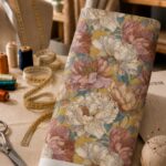 Oversized ivory and dusty rose blooms with muted teal foliage over a warm mustard background.