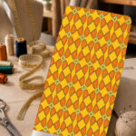 Vibrant geometric print with repeating orange petal shapes and small floral accents on a bright yellow background.