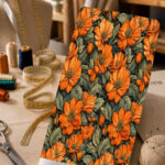 Bold orange floral print with lush muted green leaves on a deep dark background.