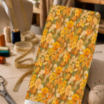 Retro floral print in warm orange, mustard, cream, and green tones on a brown background.